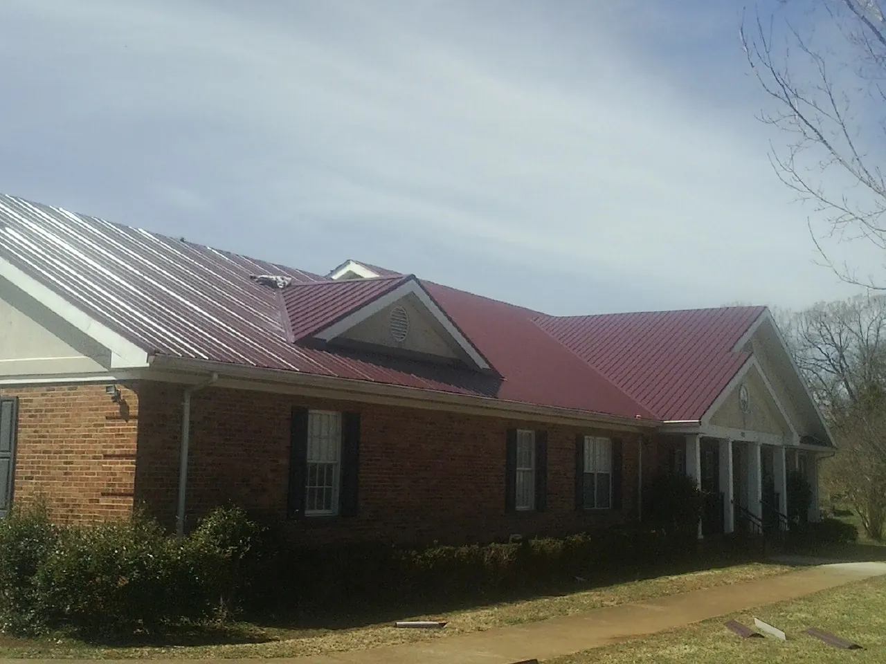 Red metal roof with gabled entries on a long brick building, from a Hail Damage Roof Repair job in Lockport